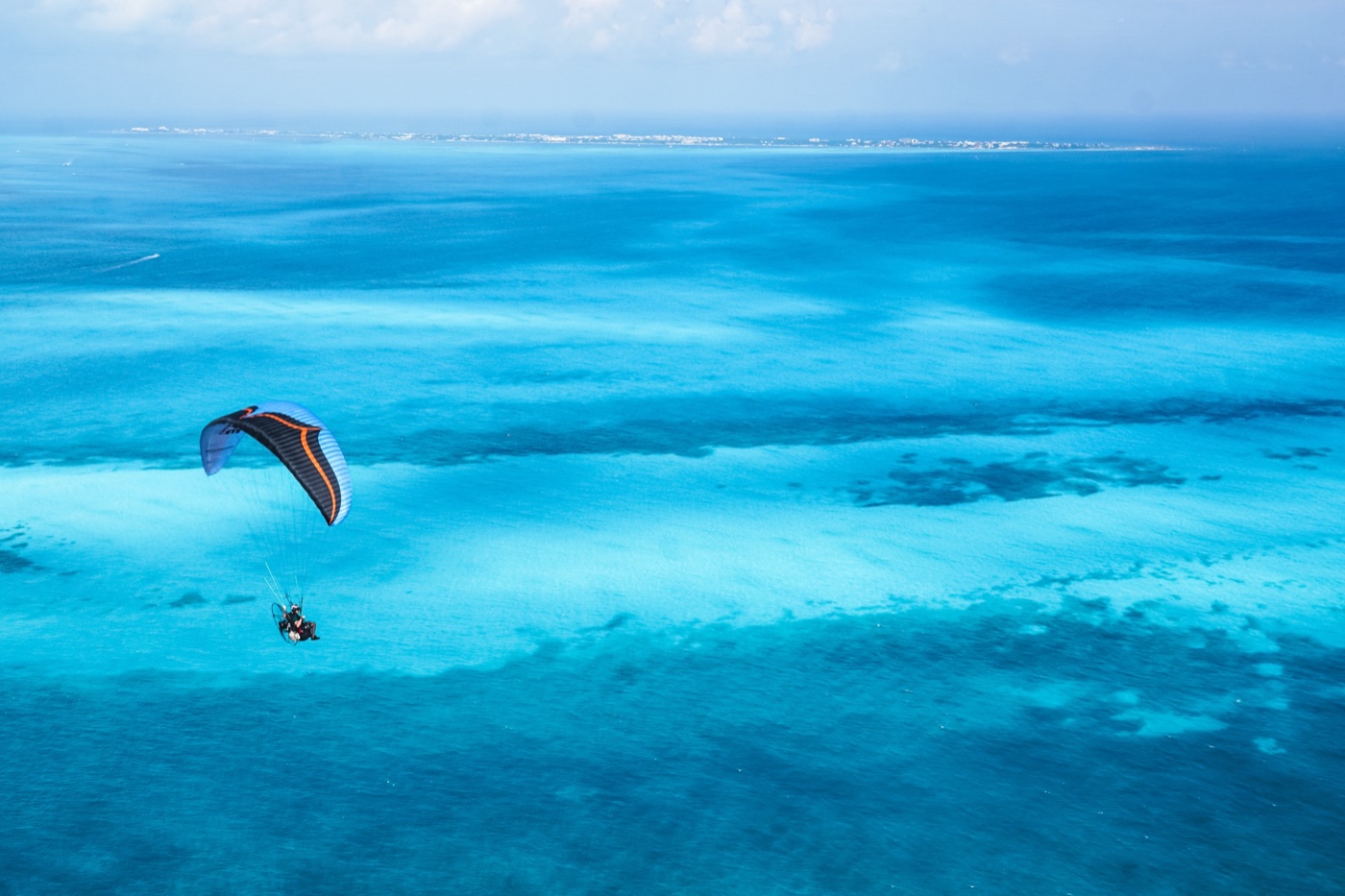 Paramotor pilot flying over turquoise water